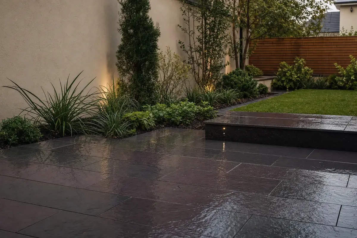 Dark riven slate patio in charcoal and plum tones beside a rendered wall in a modern British garden.